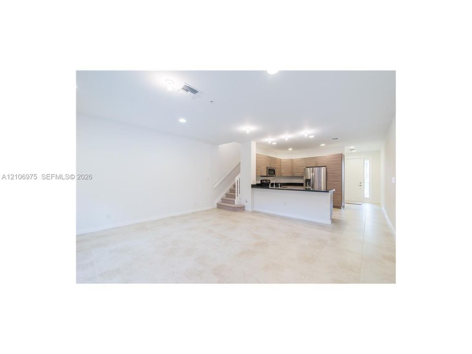 Open-concept floor plan featuring tile flooring, a kitchen peninsula with a dark countertop, recessed lighting, and wood-finish cabinetry