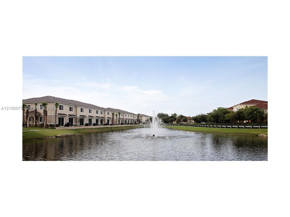 Waterfront property featuring a central fountain, manicured lawn, palm landscaping, and multi-unit buildings with neutral stucco exteriors