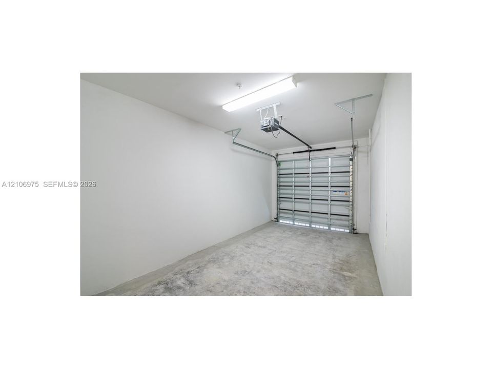 Attached garage featuring concrete flooring, finished white walls, a metal roll-up door, and overhead fluorescent lighting