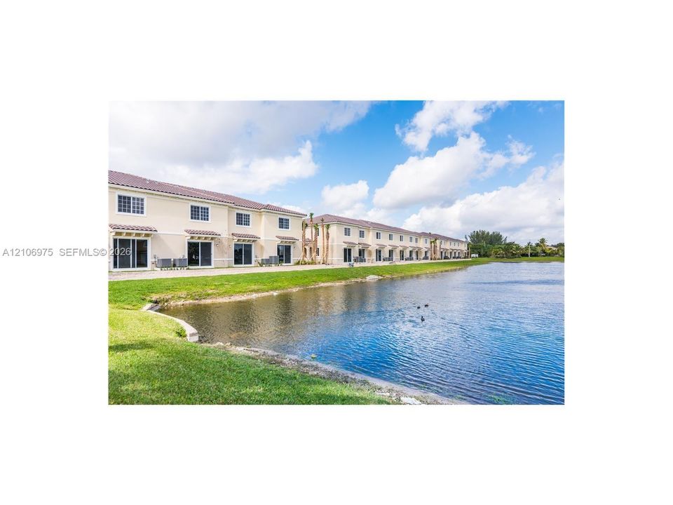 Multi-unit structure with neutral stucco exterior, tile roofing, glass sliding doors, and water frontage on a landscaped pond