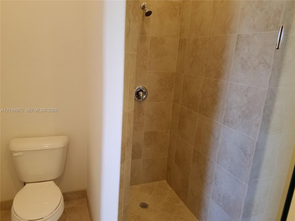 Shower enclosure featuring tile surround, wall-mounted faucet, and overhead shower head, paired with a standard-height toilet