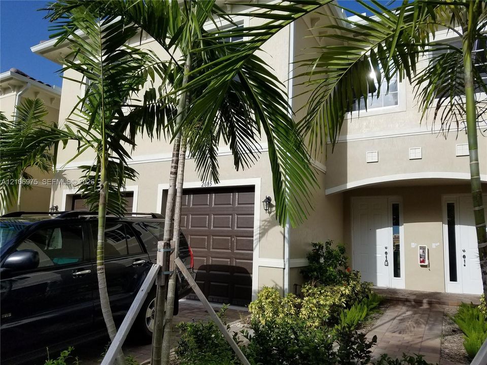 Two-story stucco exterior featuring a stone-paved walkway, paneled garage door, and decorative window glass accents