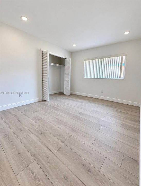 Neutral-toned wood-finish flooring, recessed lighting, and a closet with louvered bi-fold doors