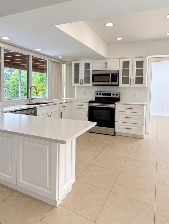 Kitchen featuring white Shaker-style cabinetry, quartz countertops, stainless steel appliances, tile flooring, and glass-paneled upper cabinets