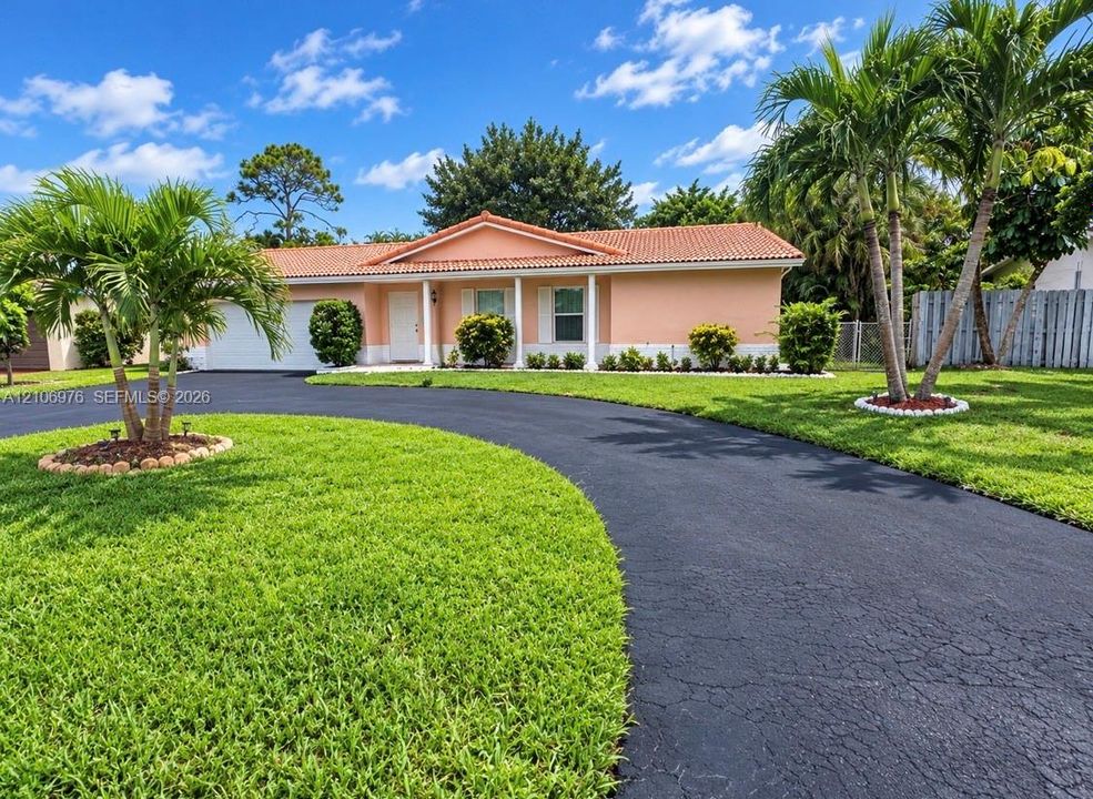 Single-story residence featuring a tile roof, covered front entrance with structural columns, and an expansive paved circular driveway situated on a landscaped lot with palm trees
