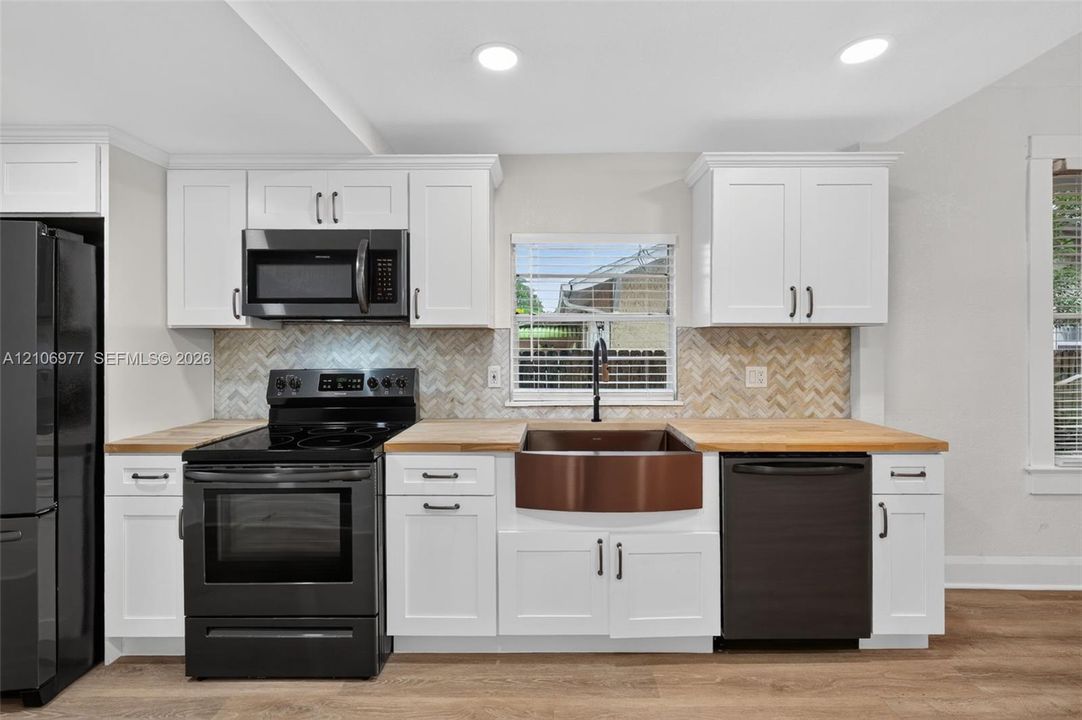 Kitchen featuring white cabinetry, butcher block countertops, a copper farmhouse sink, a herringbone-patterned tile backsplash, and black appliances