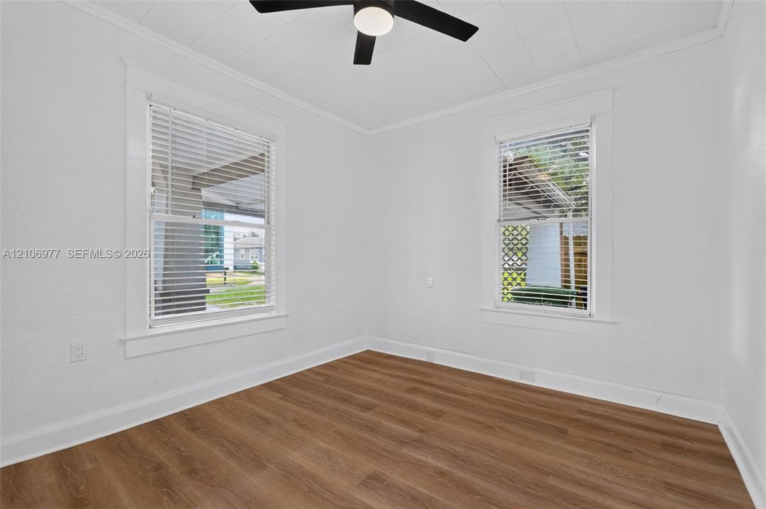 Room featuring wood-finish flooring, white walls, dual windows with blinds, and a matte black ceiling fan