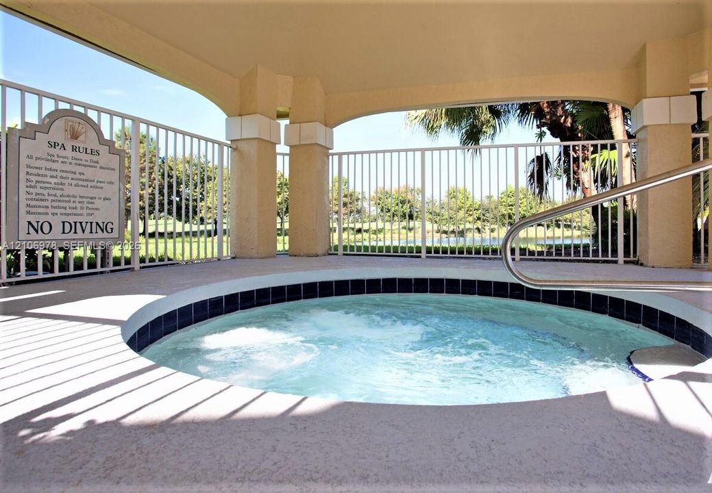 In-ground spa featuring a tiled border, concrete surround, metal safety railing, and covered patio structure