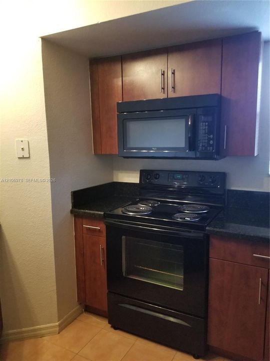 Kitchen featuring stained wood cabinetry, black countertops, and black built-in appliances including a range and microwave