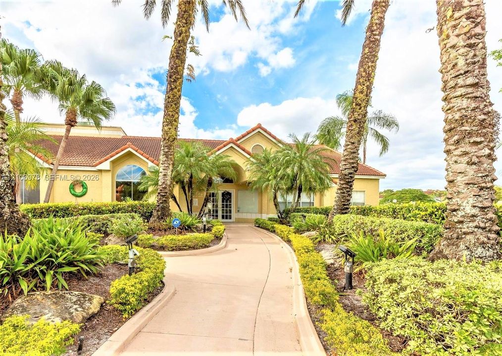 Stucco exterior featuring a tile roof, arched window, paved walkway, and mature palm trees