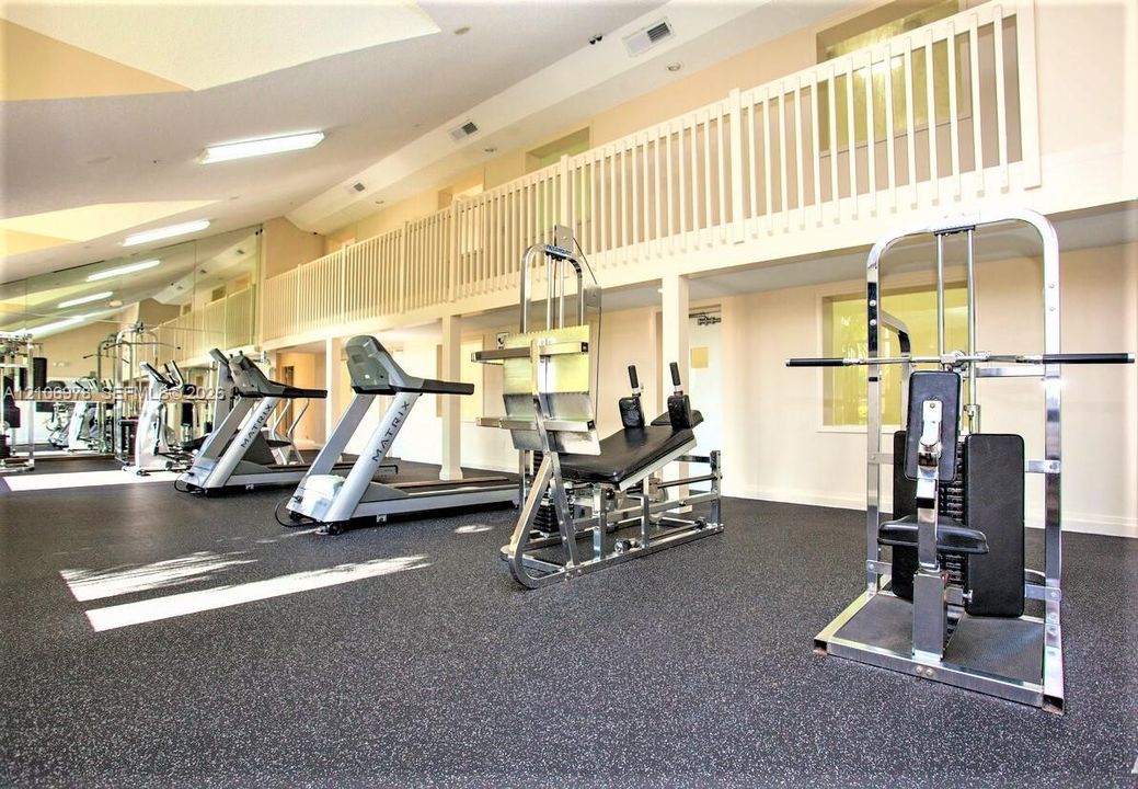 Fitness area featuring high ceilings, rubberized flooring, large mirrored wall panels, and an open loft gallery with white spindle railings