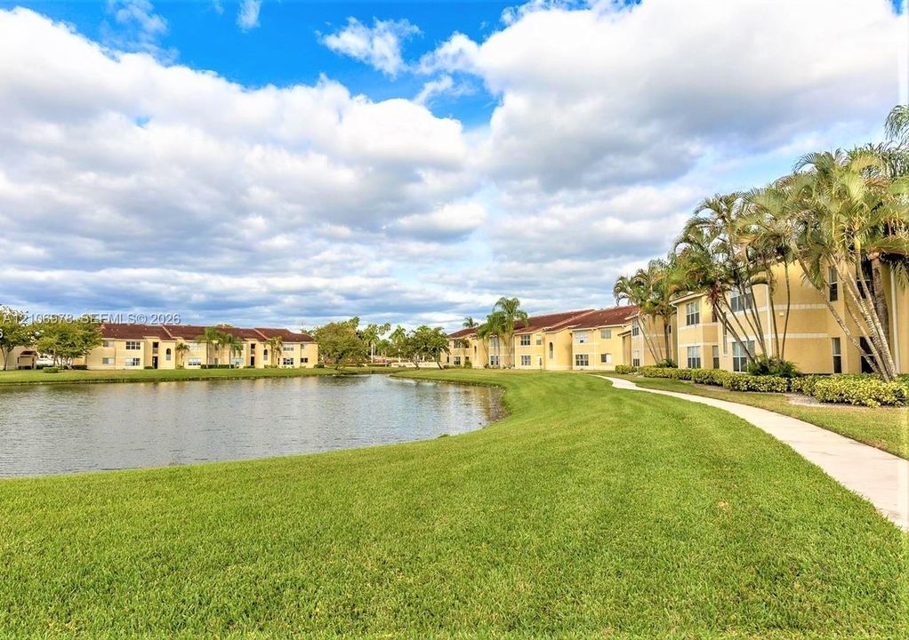 Multi-unit buildings featuring stucco exteriors, concrete tile roofing, manicured green space, a lake, and a paved walkway