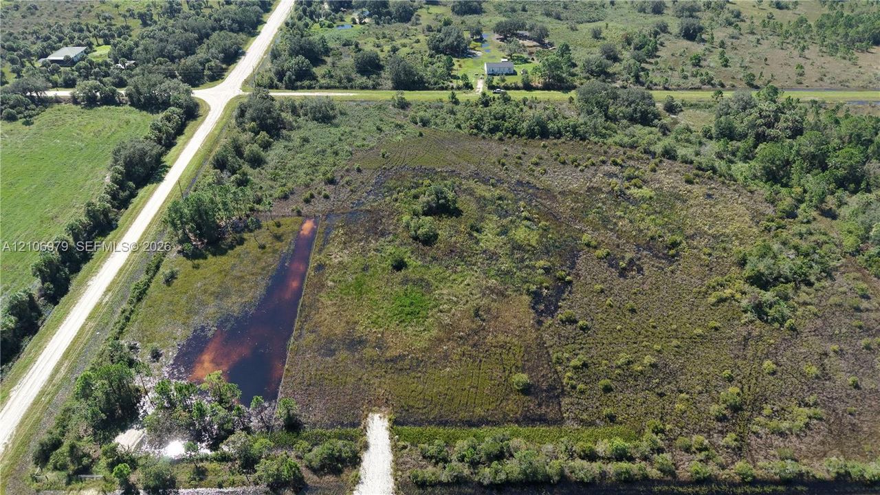 Aerial perspective of expansive acreage featuring native vegetation, scattered mature trees, and an existing water feature