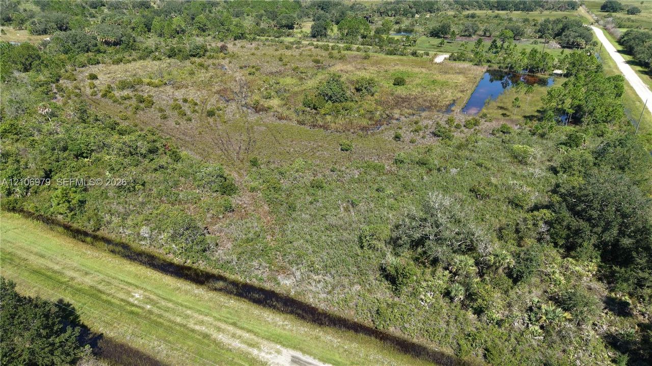 Expansive acreage featuring native vegetation, scattered mature trees, a natural pond, and paved road access