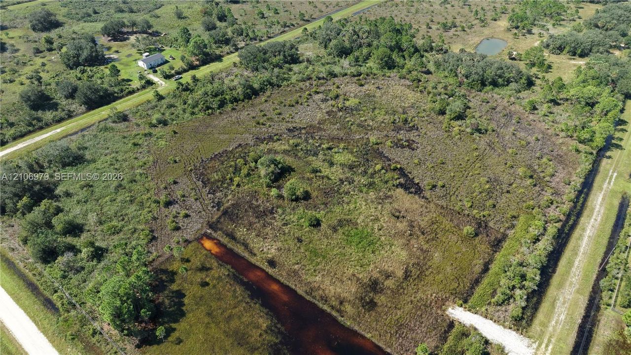 Expansive unimproved acreage featuring native vegetation, a perimeter drainage canal, and direct road access