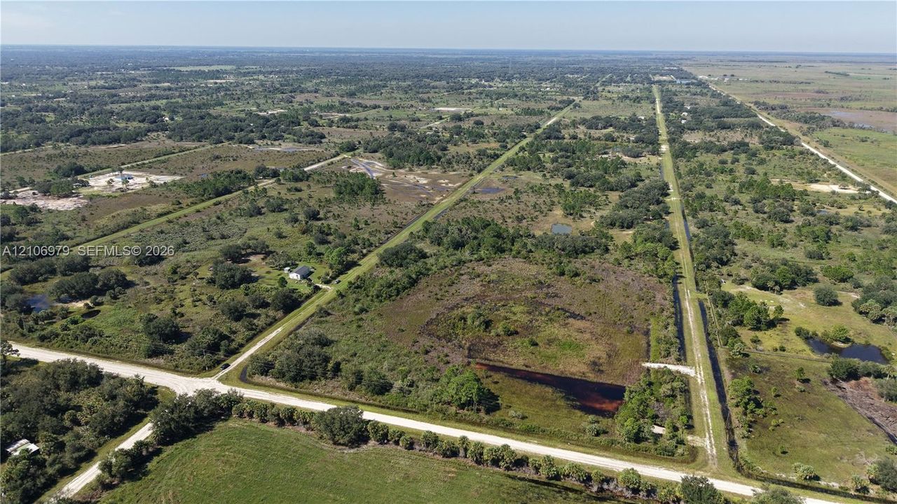 Aerial perspective of expansive rural acreage featuring mature vegetation, natural water features, and direct frontage on a gravel road