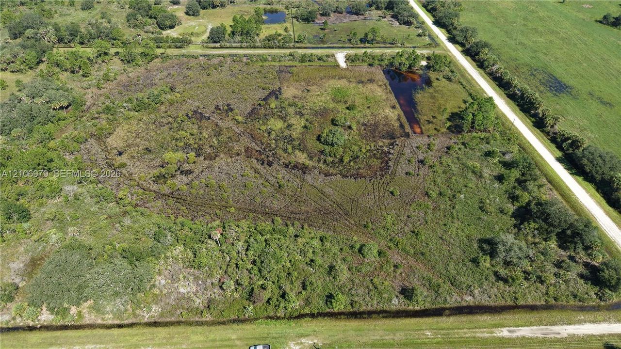 Expansive parcel of land featuring natural vegetation, mature trees, open acreage, and a water feature