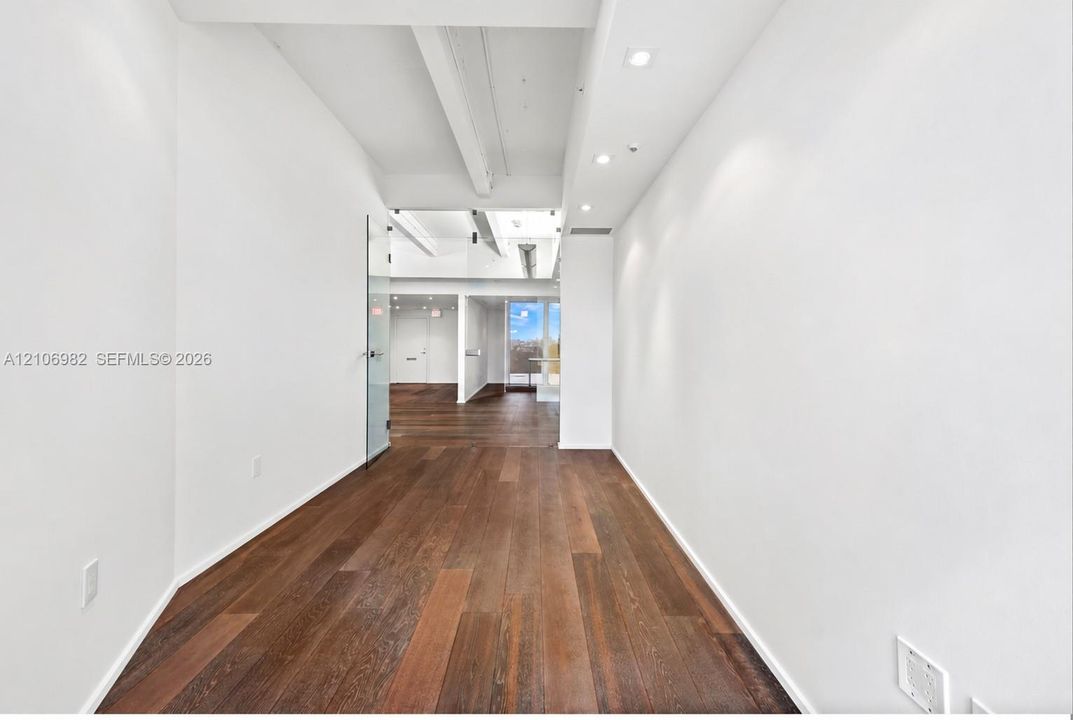 Interior hall featuring wood-finish flooring, exposed structural ceiling beams, recessed lighting, and a floor-to-ceiling glass door