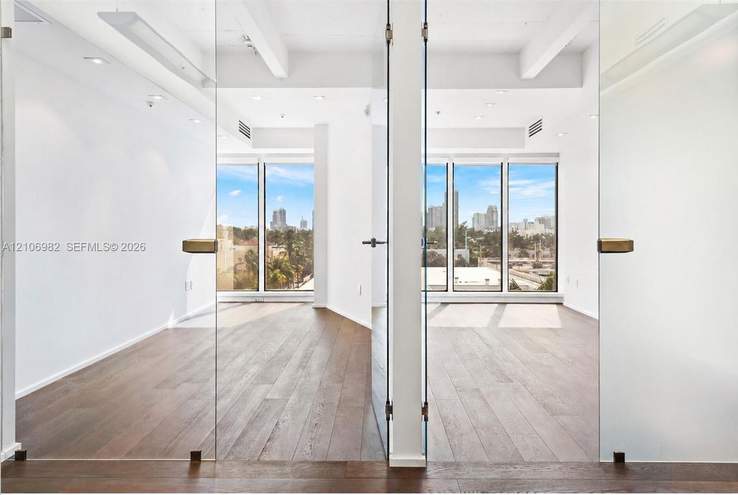 Frameless glass pivot doors, floor-to-ceiling windows, wood-finish flooring, recessed lighting, and exposed structural beams