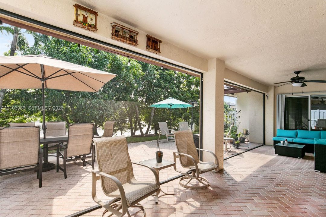 Covered patio featuring herringbone-patterned brick pavers, ceiling-mounted paddle fan, and large-format sliding glass door system