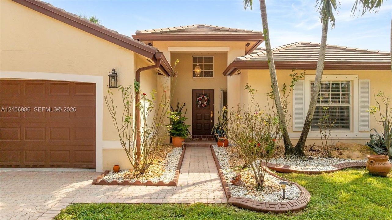 Stucco exterior with a tiled roof, paver driveway, walkway, recessed entryway, and attached garage
