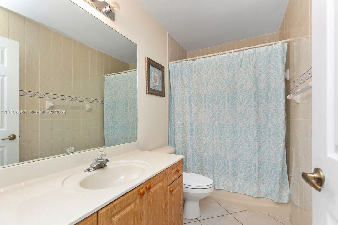 Bathroom featuring a vanity with a white countertop and integrated sink, a full-width wall mirror, tile flooring, and a tiled shower surround