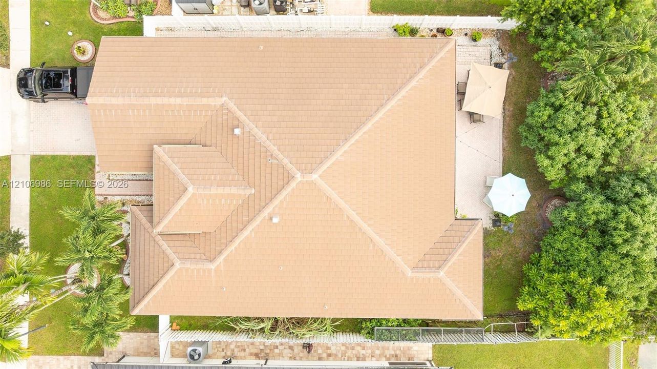 Aerial perspective of a property featuring a multi-pitch tile roof, a paved rear patio, and established perimeter landscaping