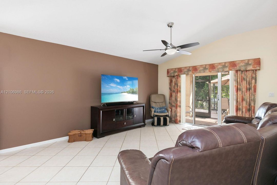 Living area with vaulted ceilings, neutral tile flooring, a stainless steel and glass ceiling fan, and sliding glass doors with exterior access