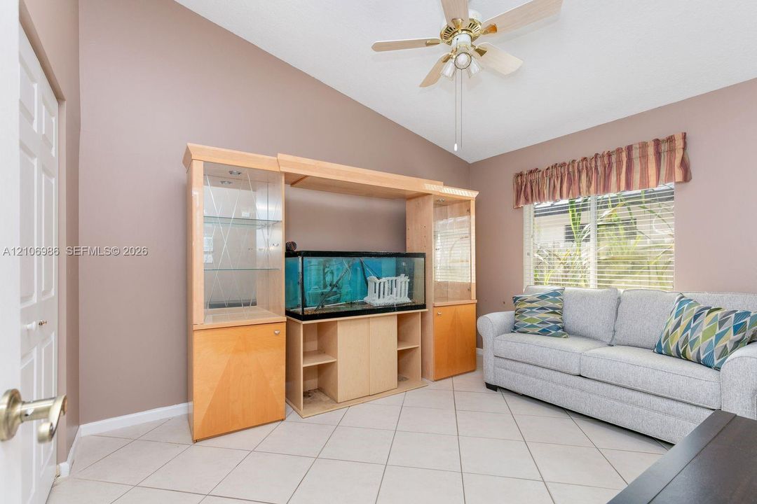 Room featuring vaulted ceilings, light-tone tile flooring, built-in wooden cabinetry with glass-paneled display shelving, and a ceiling fan