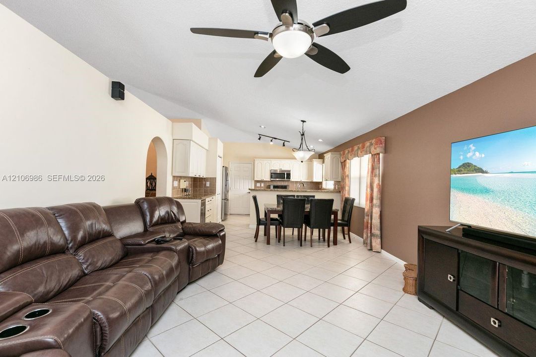 Open-concept interior featuring light-toned tile flooring, vaulted ceilings with a center-mounted ceiling fan, and track lighting