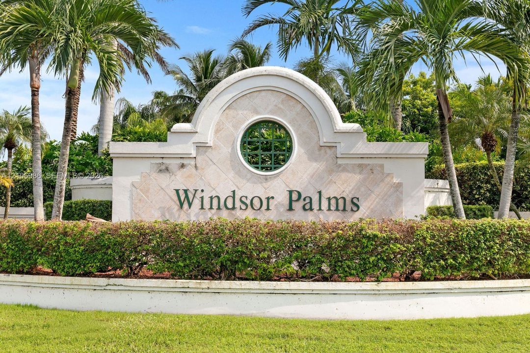 Masonry entrance monument featuring a central circular window, decorative stone-textured paneling, and a manicured perimeter of mature palm trees and sculpted shrubbery