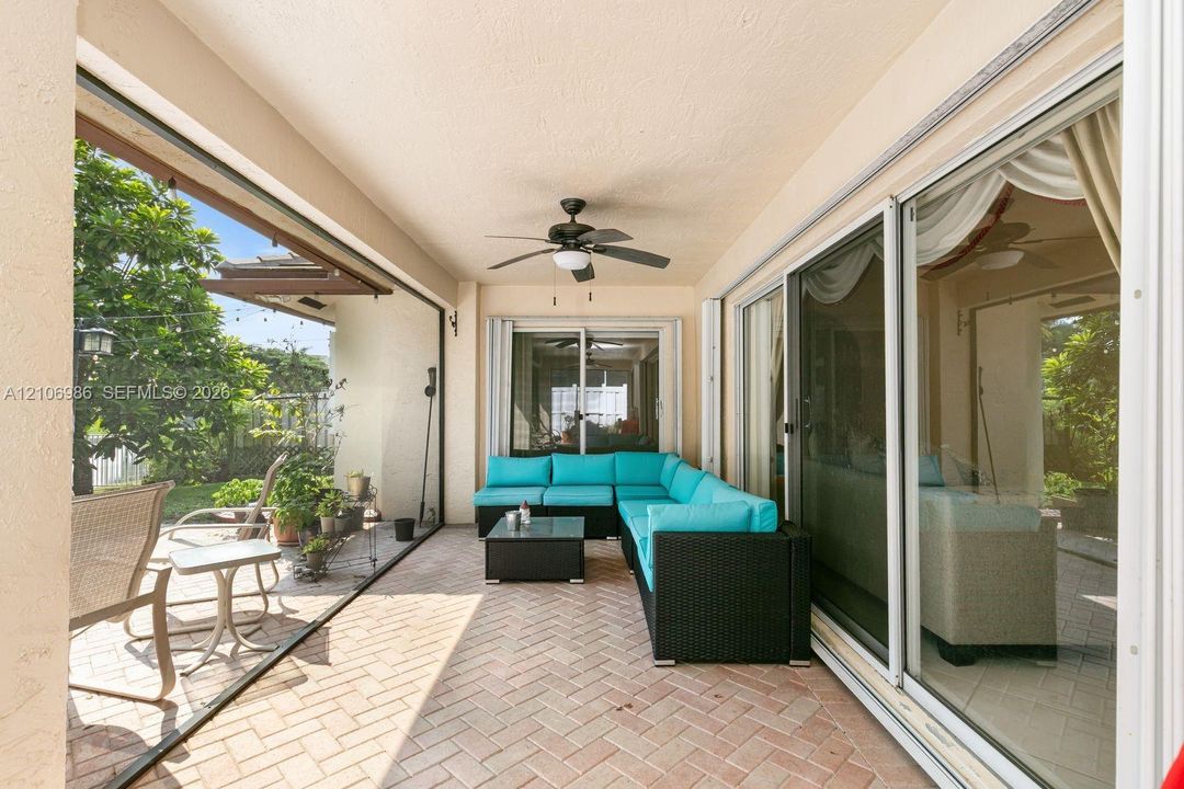 Covered outdoor patio featuring herringbone-patterned brick pavers, large multi-panel sliding glass doors, and a ceiling-mounted fan