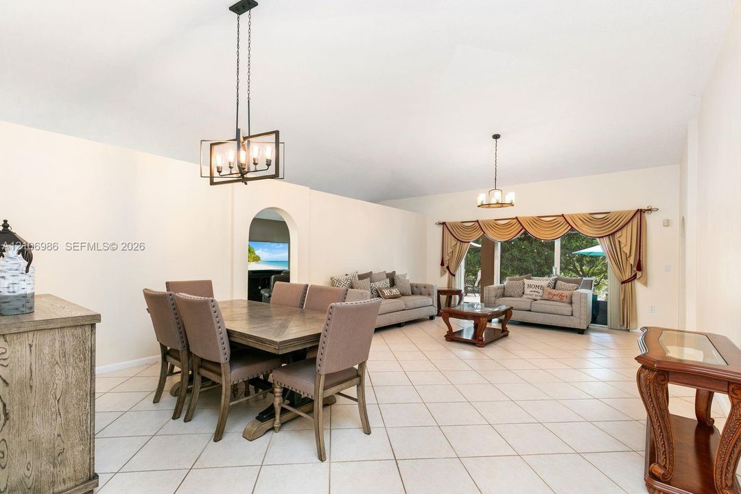 Open-concept floor plan featuring tile flooring, vaulted ceilings, dual decorative pendant light fixtures, and an arched entryway