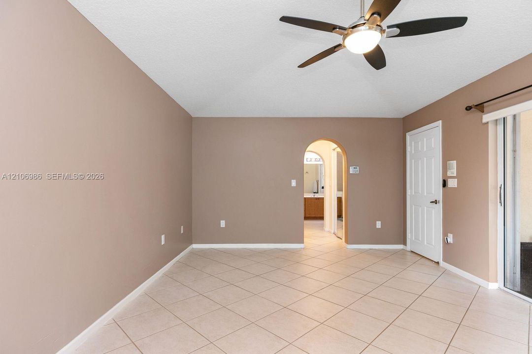Room featuring ceramic tile flooring, a multi-blade ceiling fan with integrated lighting, a structural arched doorway, and a sliding glass door