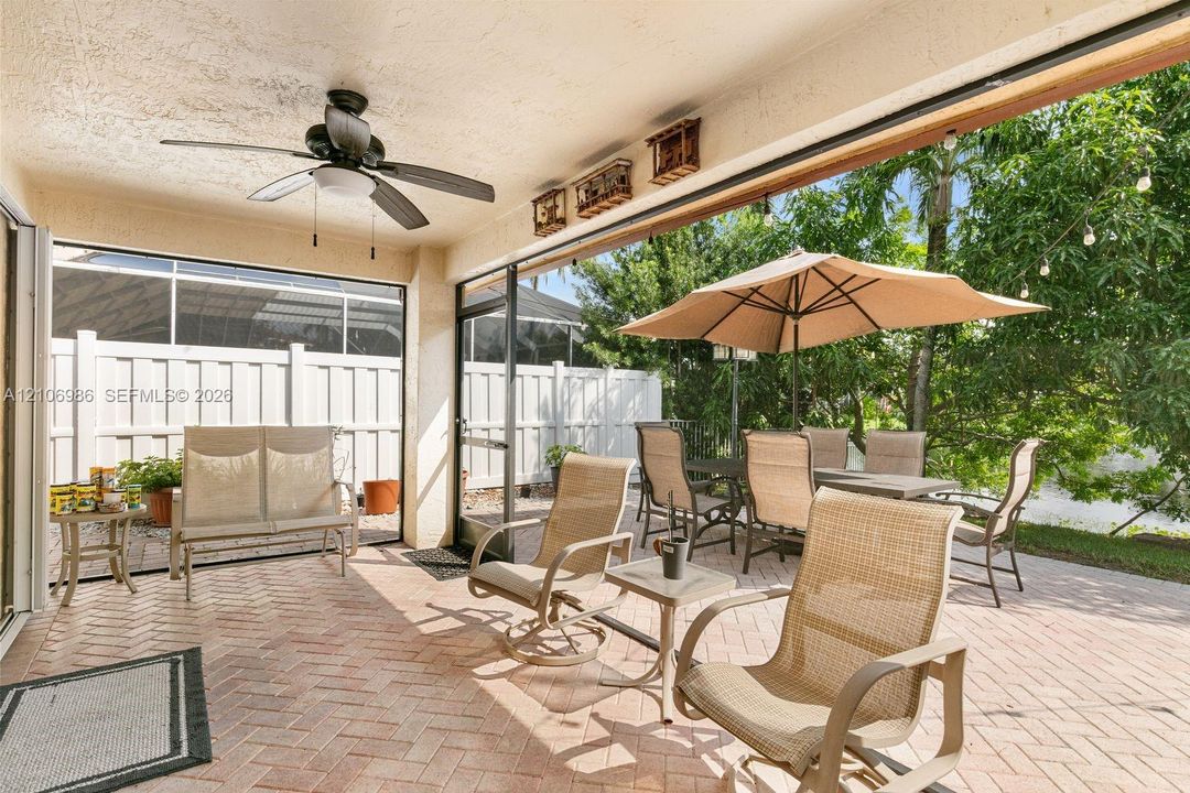 Covered patio featuring brick paver flooring, integrated ceiling fan, and screened enclosure