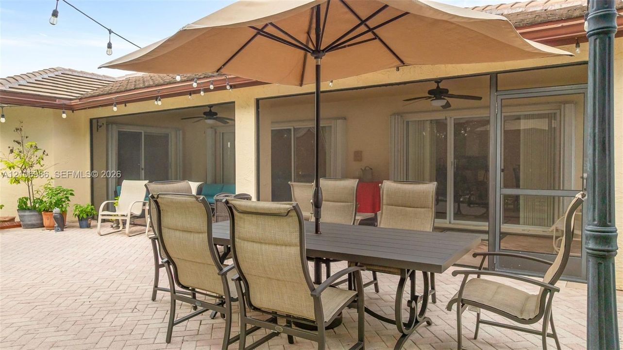 Covered patio featuring a paved brick surface, screen enclosure, and ceiling fans