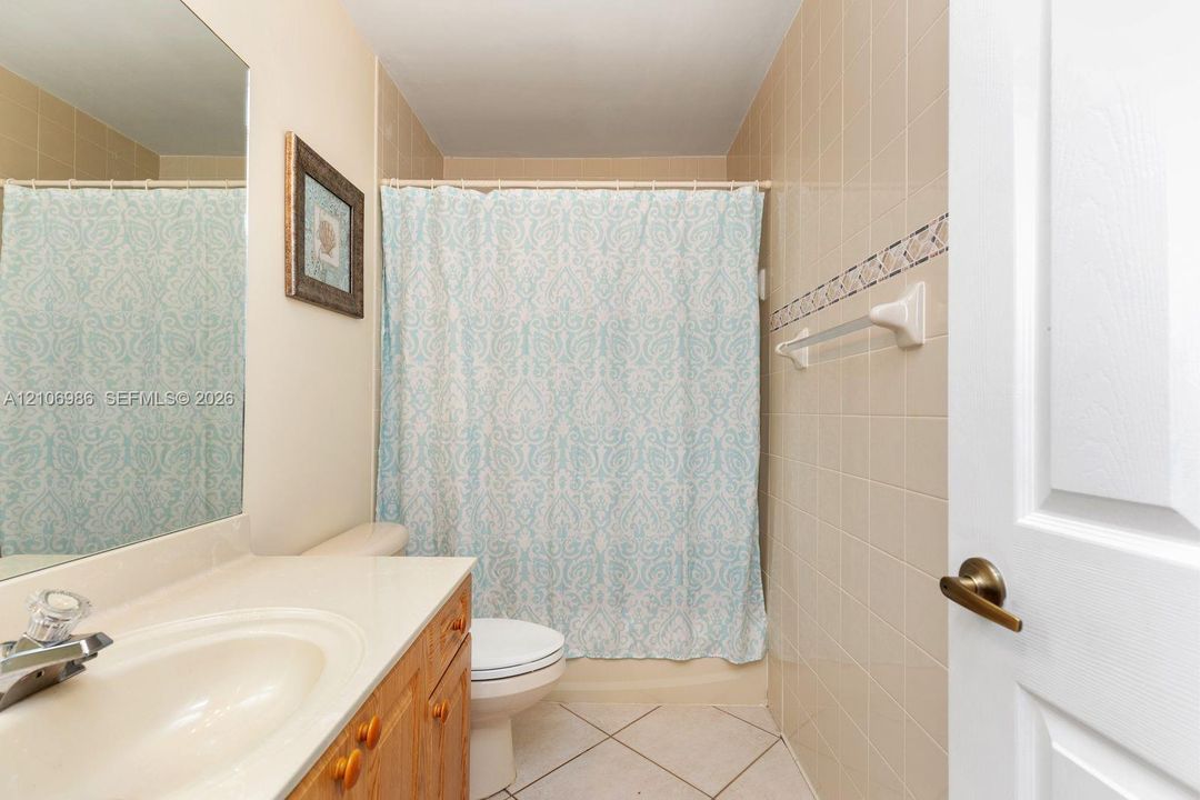 Bathroom featuring a wooden vanity with a stone countertop, an integrated sink, a large wall-mounted mirror, and tile flooring with decorative wall tile accents