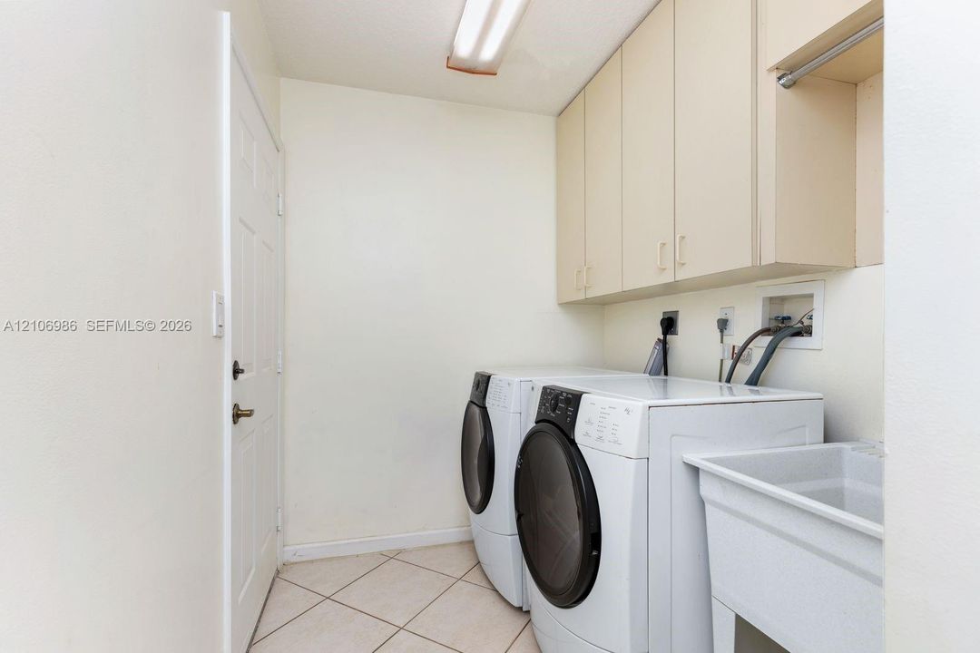 Laundry area featuring built-in upper cabinetry, utility sink, tile flooring, and overhead lighting
