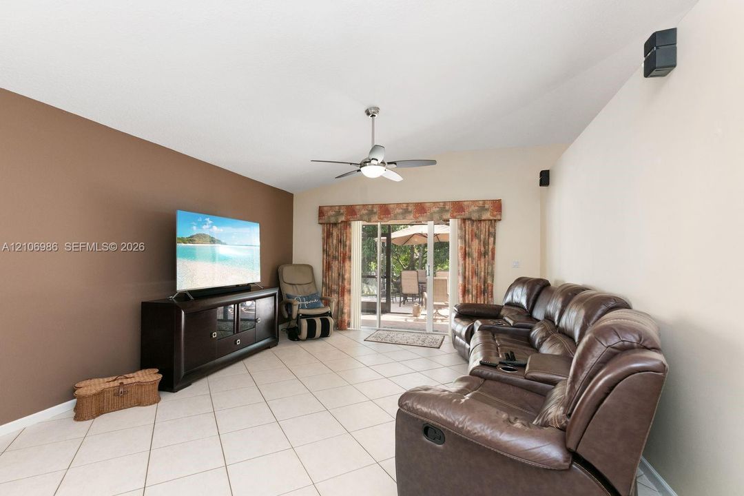 Living space featuring vaulted ceilings, neutral ceramic tile flooring, a ceiling fan with integrated lighting, and sliding glass doors