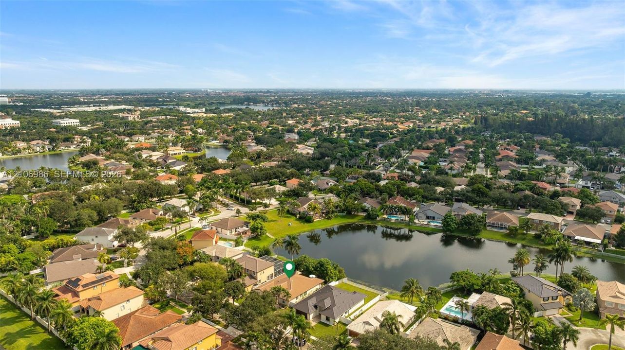 Aerial perspective of a property situated on a lakefront lot featuring a multi-pitched roofline, palm trees, and mature landscaping