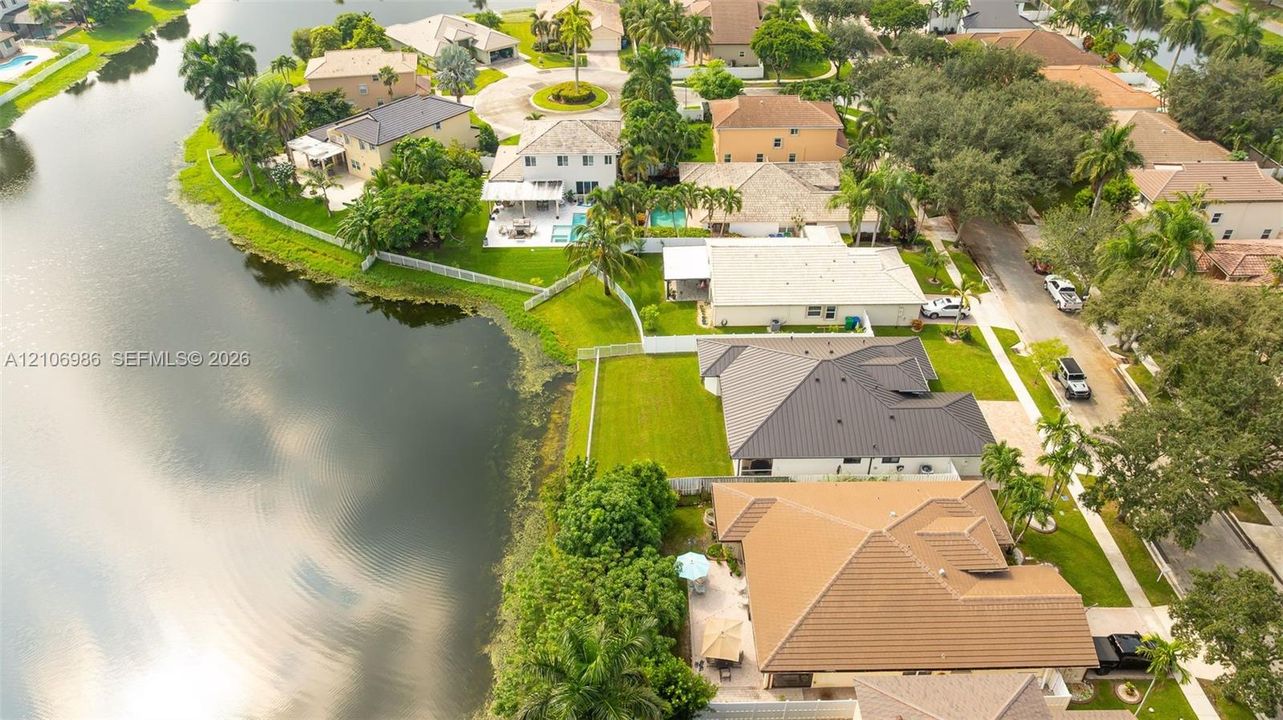 Aerial perspective of a waterfront residential area featuring mature landscaping, tile-roofed properties, private fenced backyards, and expansive water frontage