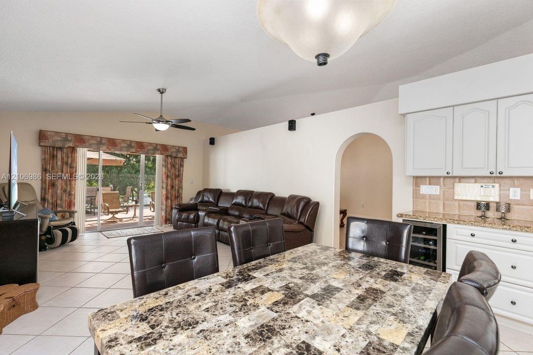 Vaulted ceilings, built-in beverage refrigerator, arched doorway, ceiling fan, and sliding glass doors