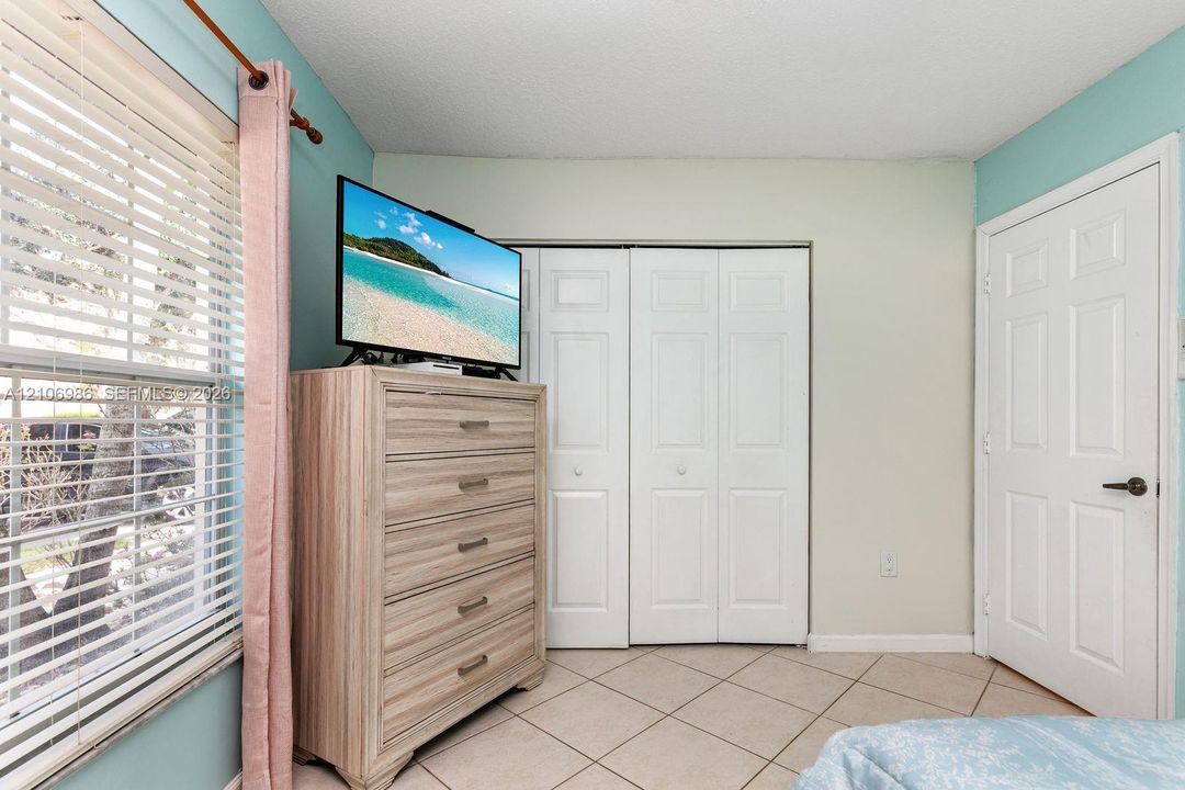 Ceramic tile flooring arranged in a diagonal pattern, white paneled bi-fold closet doors, a classic six-panel interior door, and a window with horizontal blinds