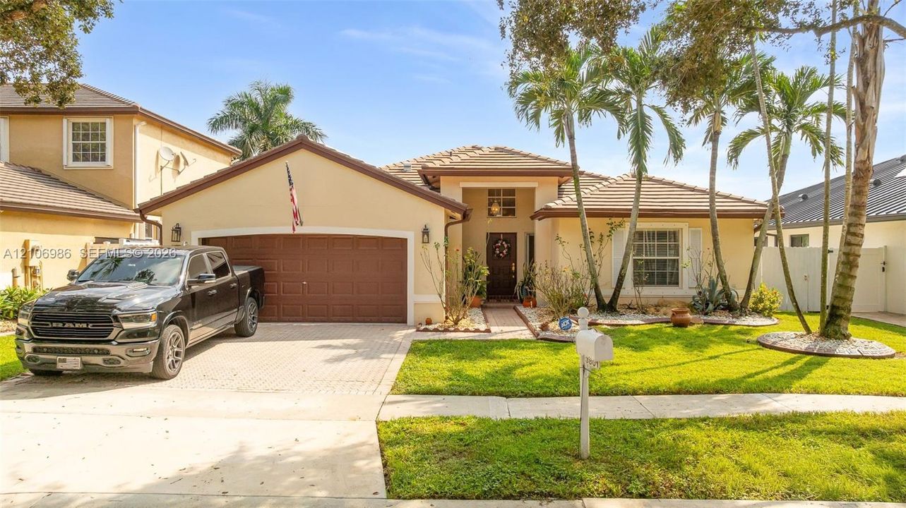 Stucco exterior residence featuring a paved driveway, a multi-car garage, tile roofing, and curated landscaping with mature palm trees