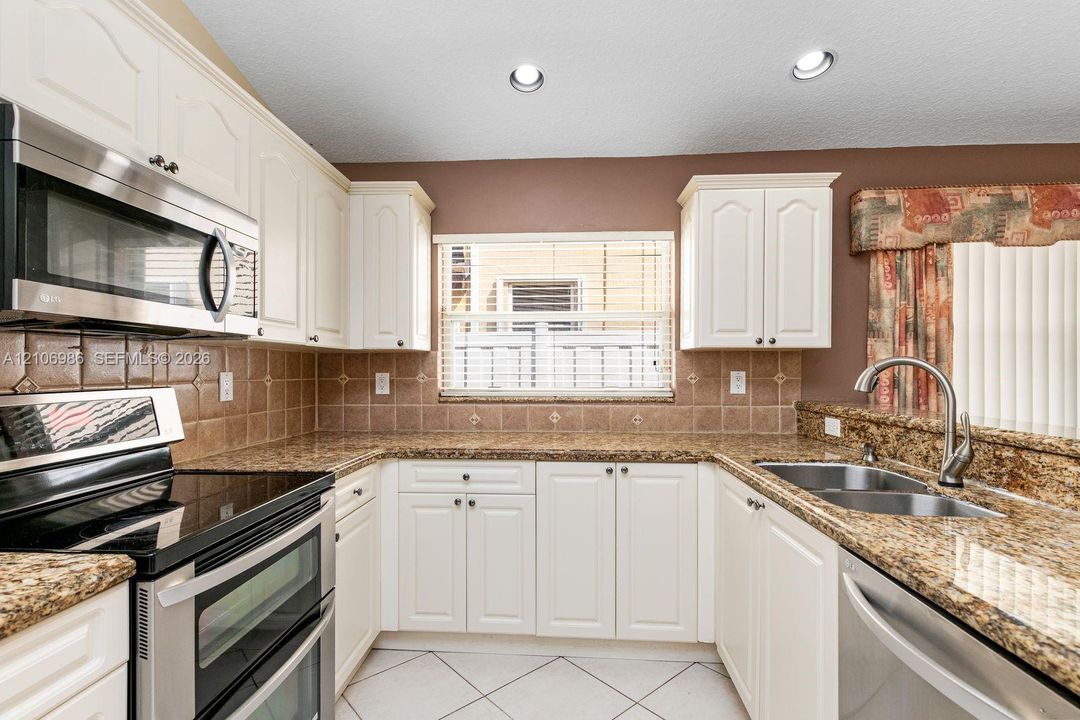 Kitchen featuring white cabinetry, stone countertops, square tile backsplash, recessed lighting, and stainless steel appliances