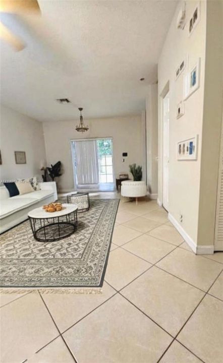 Open-concept interior featuring large-format diagonal tile flooring, high ceilings, sliding glass patio doors, and a decorative chandelier