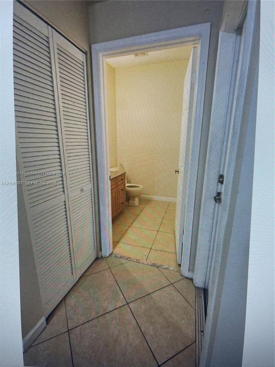 Louvered bi-fold closet doors, neutral ceramic floor tiling, and a wooden vanity cabinet