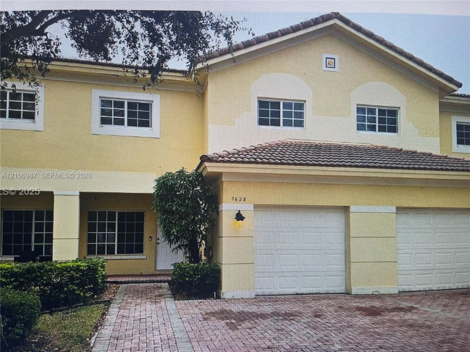 Stucco exterior featuring a dual-car garage, pitched tile roofing, multi-pane windows, and a brick-paver driveway