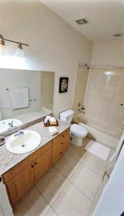 Bathroom featuring a vanity with a stone-finish countertop, oval undermount sink, three-light fixture, and light-tone tile flooring