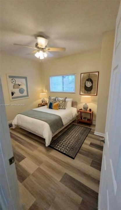 Room featuring wood-finish flooring, a central ceiling fan with integrated lighting, and a window with blinds